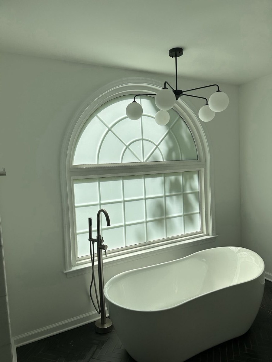 Arched bathroom window with frosted privacy film above a freestanding tub